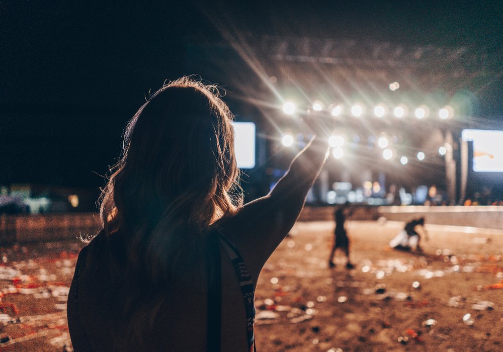 A woman raising her hand toward a lit stage at a night event