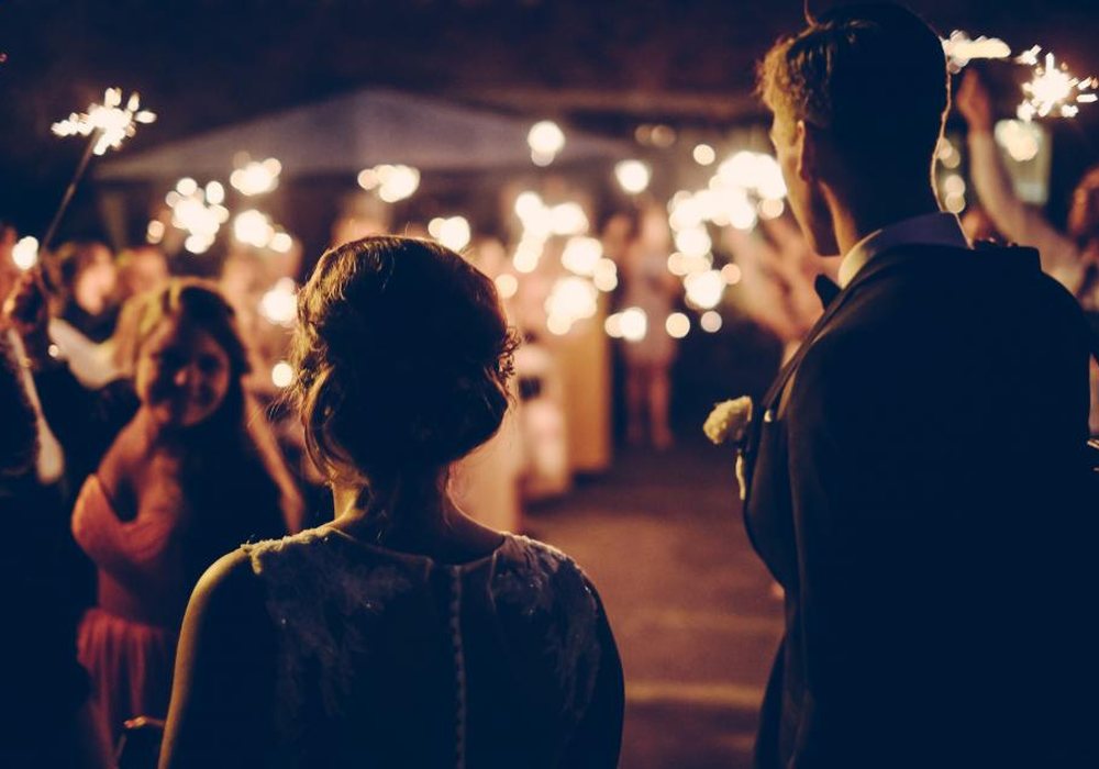 A couple walking through a crowd of guests holding sparklers at night