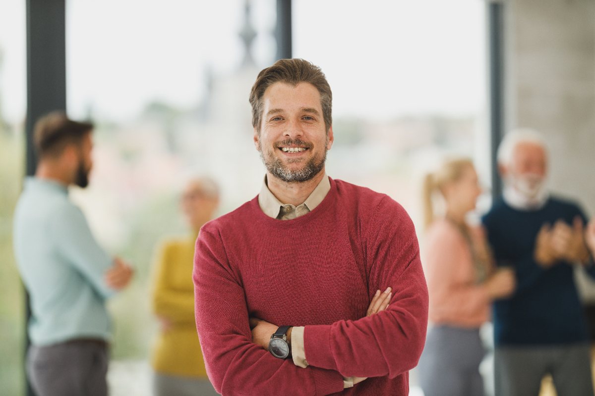 A smiling man in a red sweater with his arms crossed