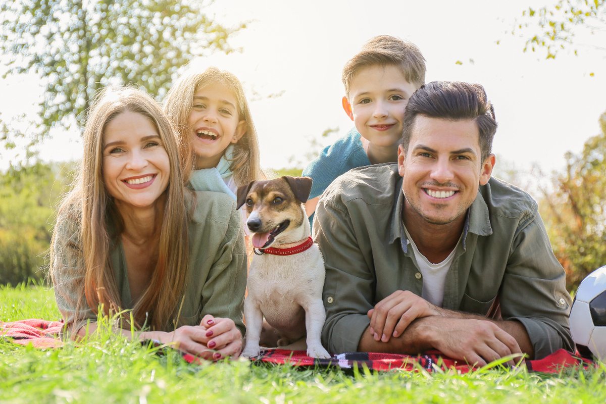 A smiling family with two children and their dog lying together on the grass