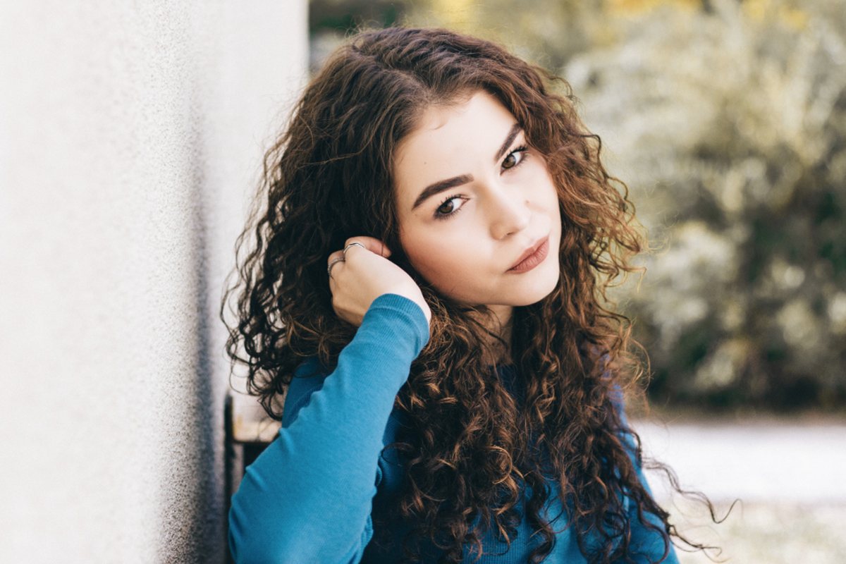 A young woman with curly hair resting her head against a wall